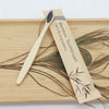 A bamboo toothbrush is shown lying on a wooden board with dried plant material.