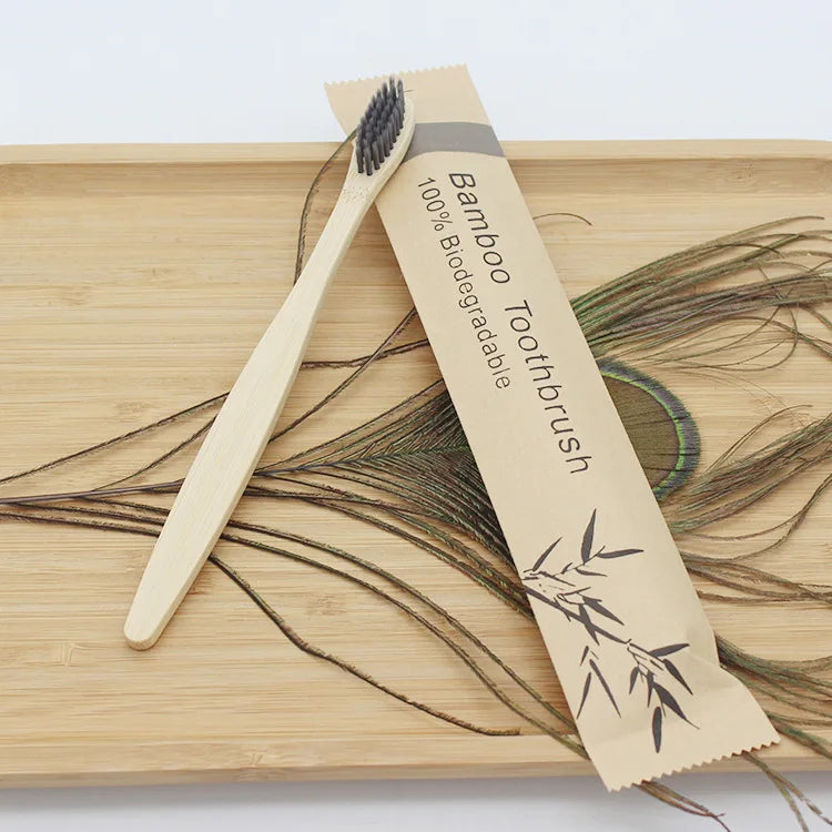 A bamboo toothbrush is shown lying on a wooden board with dried plant material.