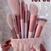 A collection of 13 professional makeup brushes in various shades of pink and nude are displayed on a white fluffy surface.