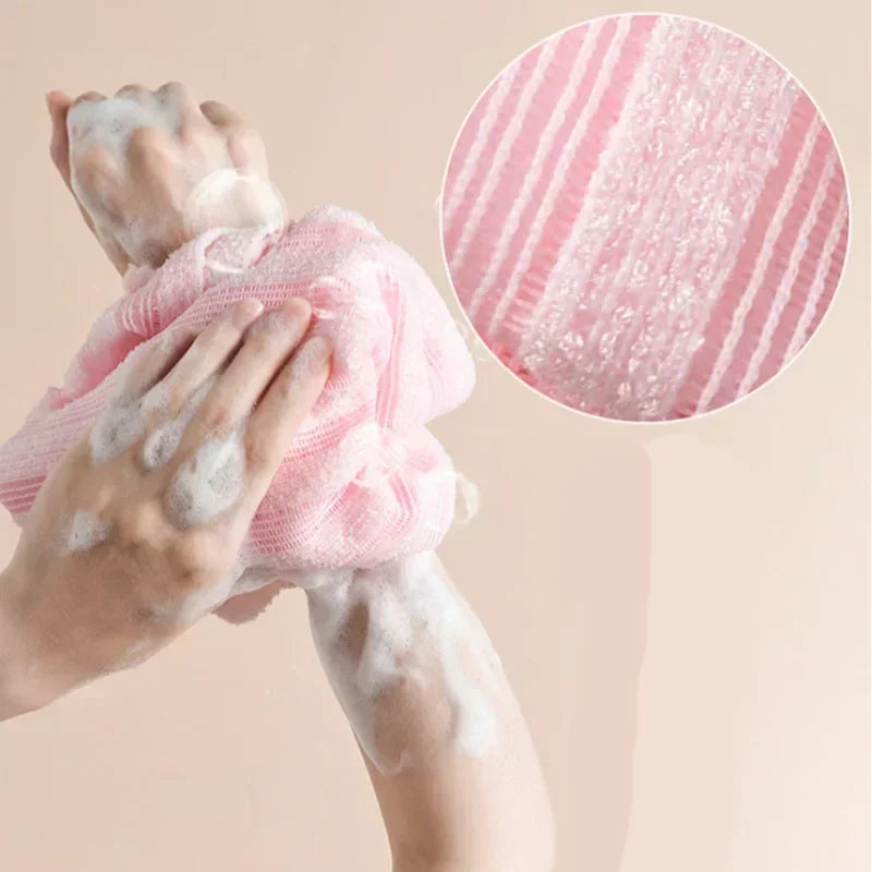 Hands are using a pink exfoliating bath towel to scrub white foam on their skin.