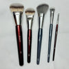 Un set de cinq pinceaux de maquillage pour fond de teint liquides à angle avec ferrules argentées et manches sombres.
