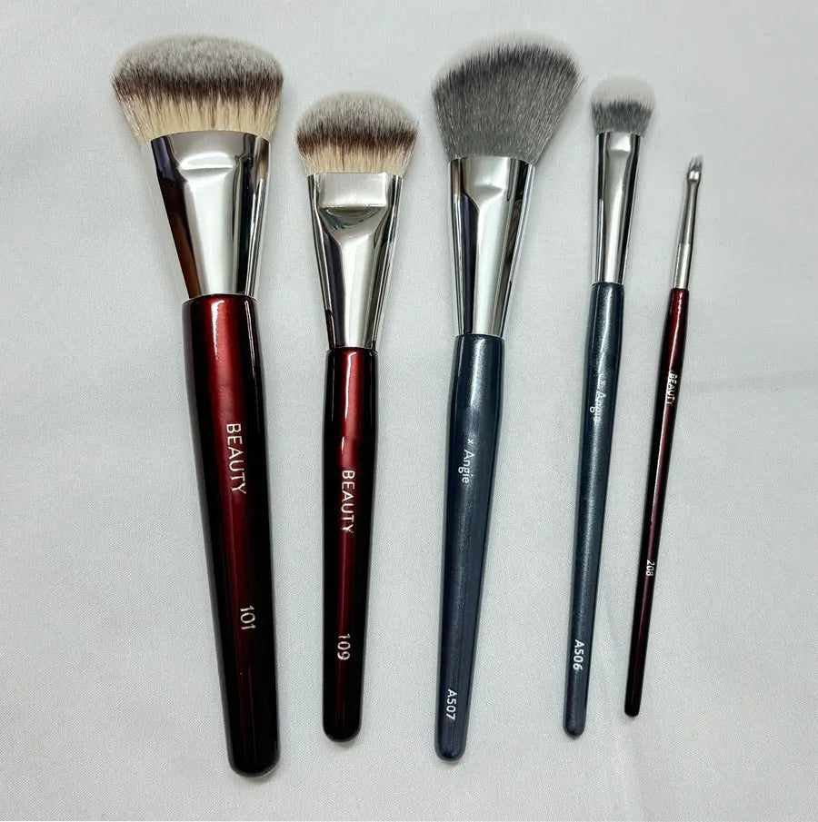 Un set de cinq pinceaux de maquillage pour fond de teint liquides à angle avec ferrules argentées et manches sombres.