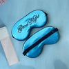 A bright blue silk sleep mask embroidered with the text Good Night is displayed next to its packaging.