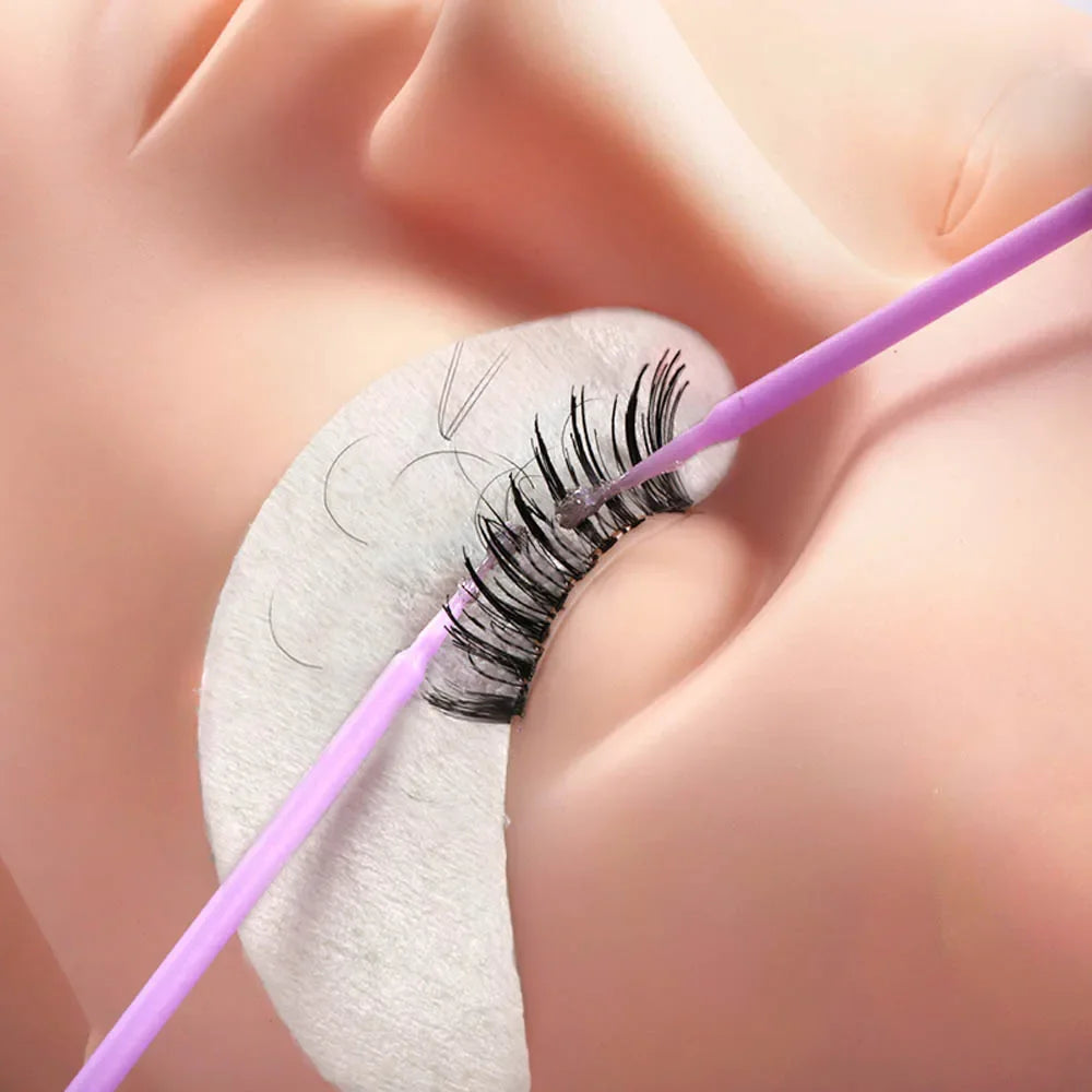 Gros plan d'un pinceau micro violet utilisé pour le travail de détail sur une cils.