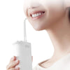A person is using a white portable cordless oral irrigator with a thin nozzle to clean their mouth.