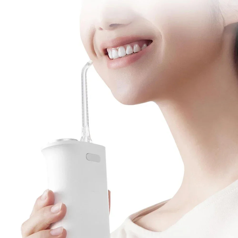 A person is using a white portable cordless oral irrigator with a thin nozzle to clean their mouth.