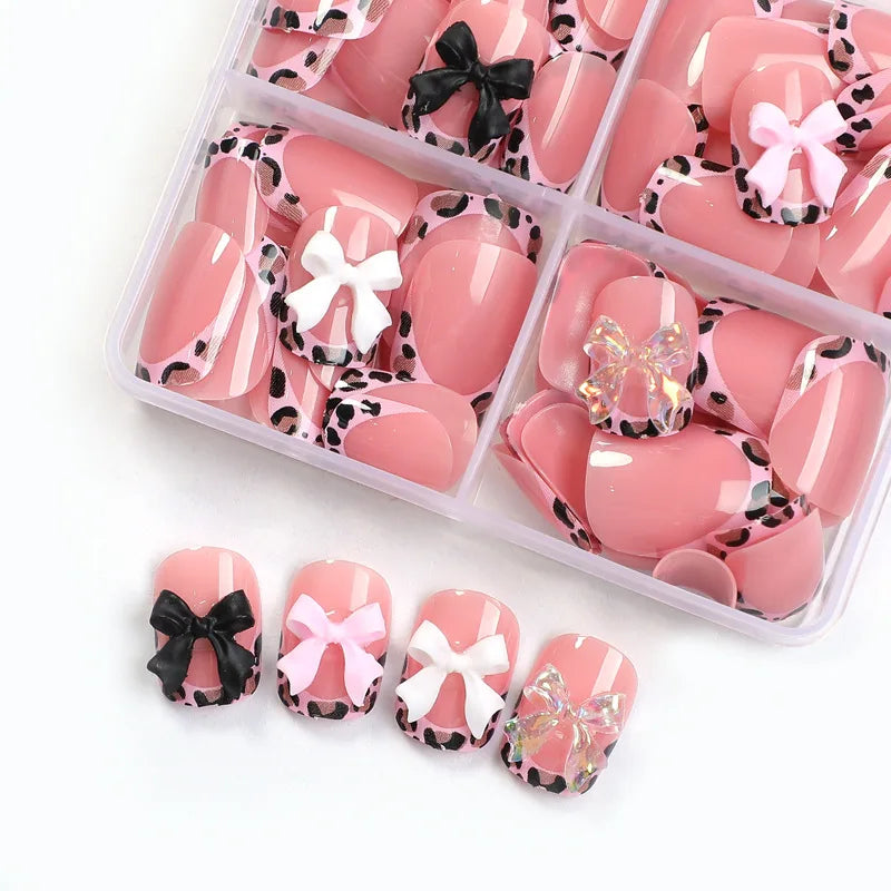 A box of pink and white leopard print press-on nails with various bow designs.
