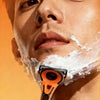 A close-up of a man shaving his face with an orange precision safety razor featuring a 6-layer blade system.