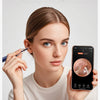 A woman holds a smartphone displaying an internal view of an ear, while another hand holds a medical instrument near her ear.