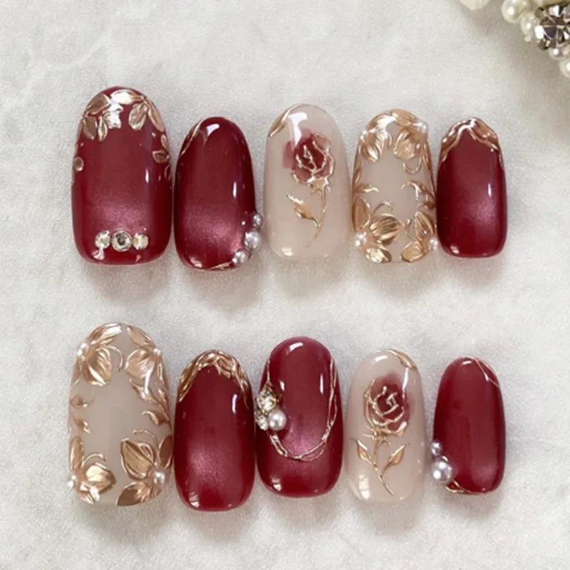 A set of 24 press-on almond nails featuring a deep burgundy color with delicate gold floral and butterfly designs.