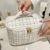 A hand is opening a beige knitted canvas makeup pouch with gold hardware.