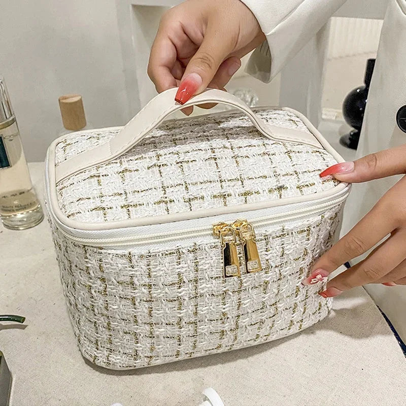 A hand is opening a beige knitted canvas makeup pouch with gold hardware.