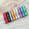 A row of colorful mini refillable perfume atomizer bottles arranged diagonally on a white marble surface.
