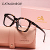 A pair of black-framed square reading glasses with a leopard print pattern resting on a pink leather clutch.