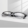 Une paire de lunettes de lecture à monture noire et multi-lentilles avec des verres clairs, posées sur une surface blanche.