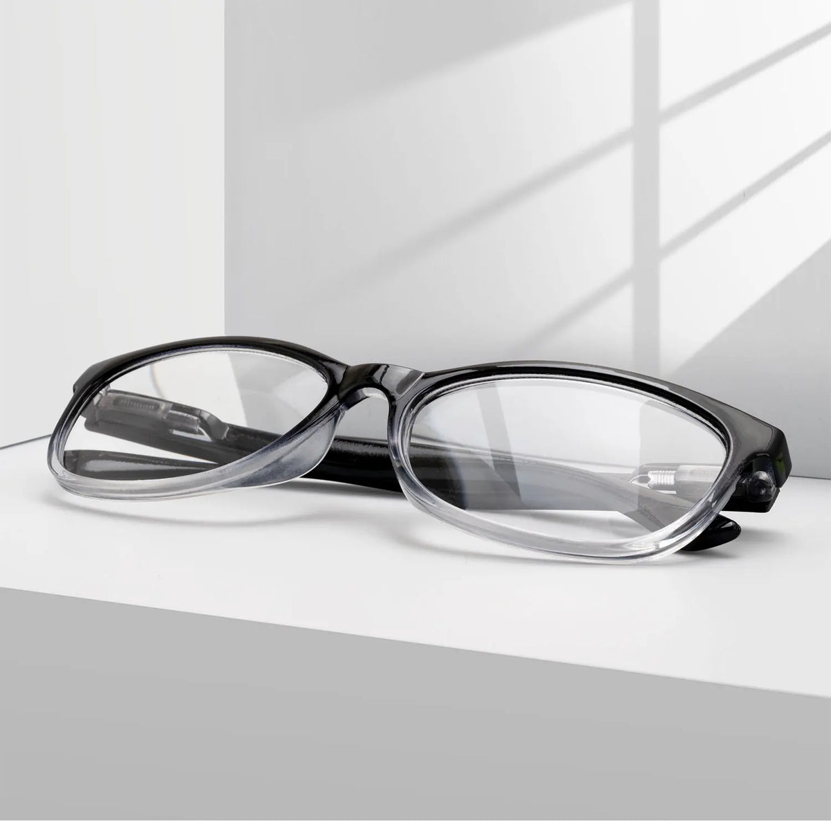 Une paire de lunettes de lecture à monture noire et multi-lentilles avec des verres clairs, posées sur une surface blanche.