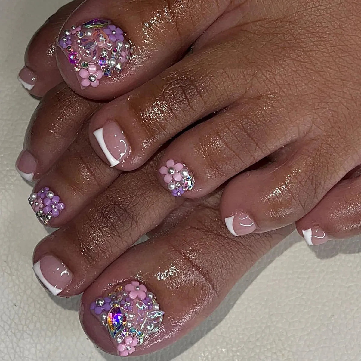 A hand displaying press-on fake nails with short square French design featuring pink and purple glitter accents.
