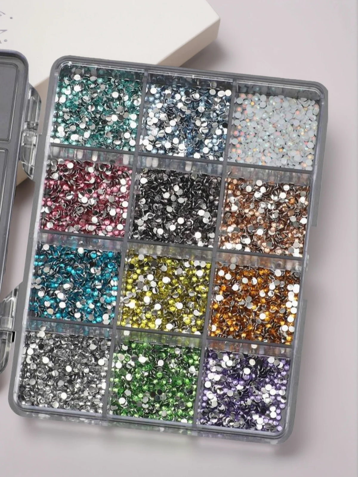 Boîte en plastique transparent remplie de strass et d'outils pour l'art des ongles en résine.