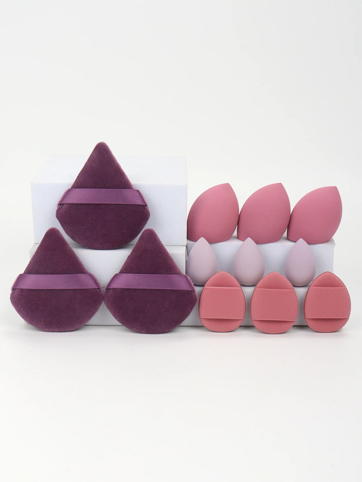 A set of twelve all-purpose makeup sponges in various shades of pink and purple, arranged on a white surface.
