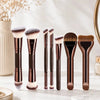 A set of seven professional makeup brushes with dark wood and gold accents displayed on a white marble surface.