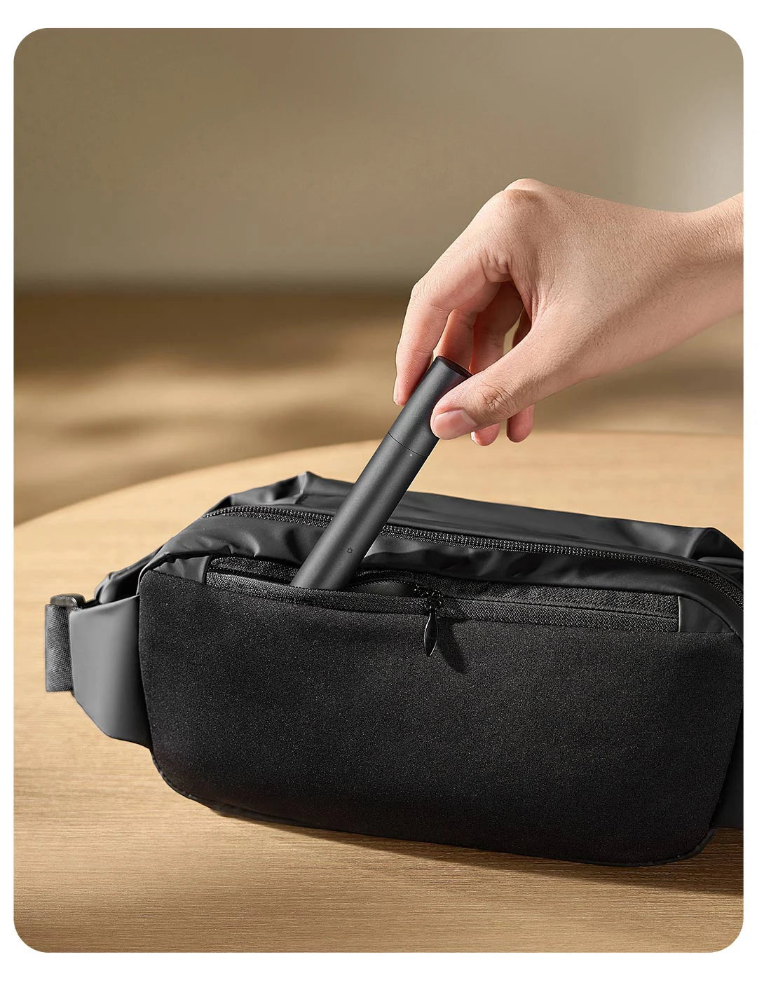 A hand is inserting a black electric nose and eyebrow hair trimmer into a black zippered pouch.