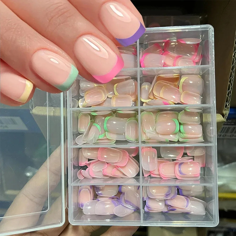 Une main tient une boîte en plastique transparent remplie de faux ongles acryliques colorés, dans différentes nuances de rose