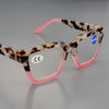 Par de gafas de lectura cuadradas con montura de estampado de leopardo y marcos rosas sobre una superficie gris.
