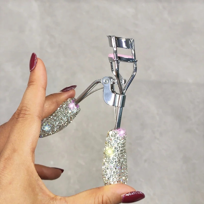 A hand holds a professional eyelash curler set with silver metal tools and glittery pink and silver tips.