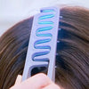 A close-up of a purple hair styling comb with a blue wavy insert being used on dark hair.