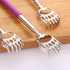 A stainless steel telescopic back scratcher with a purple handle and silver serrated fingers resting on a wooden surface.