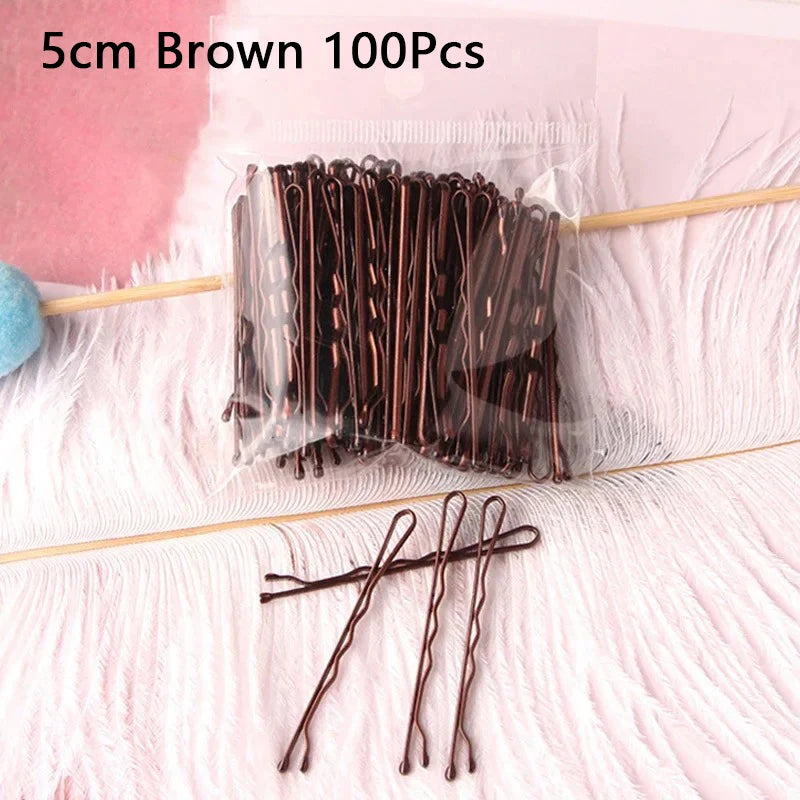 A bundle of 100 brown metal U-shaped hair pins is displayed on a pink surface.