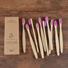 A set of ten natural bamboo toothbrushes with pink bristles arranged on a wooden surface.