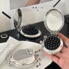 A silver folding massage comb and mirror are displayed on a white plate.