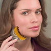 A woman holds a wooden lymphatic contour facial massage brush near her face.