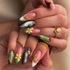 A close-up of a hand displaying a set of press-on nails featuring pink flowers and star designs on various nail shapes.