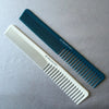 A pair of anti-static professional hair cutting combs in white and teal are laid diagonally on a gray surface.