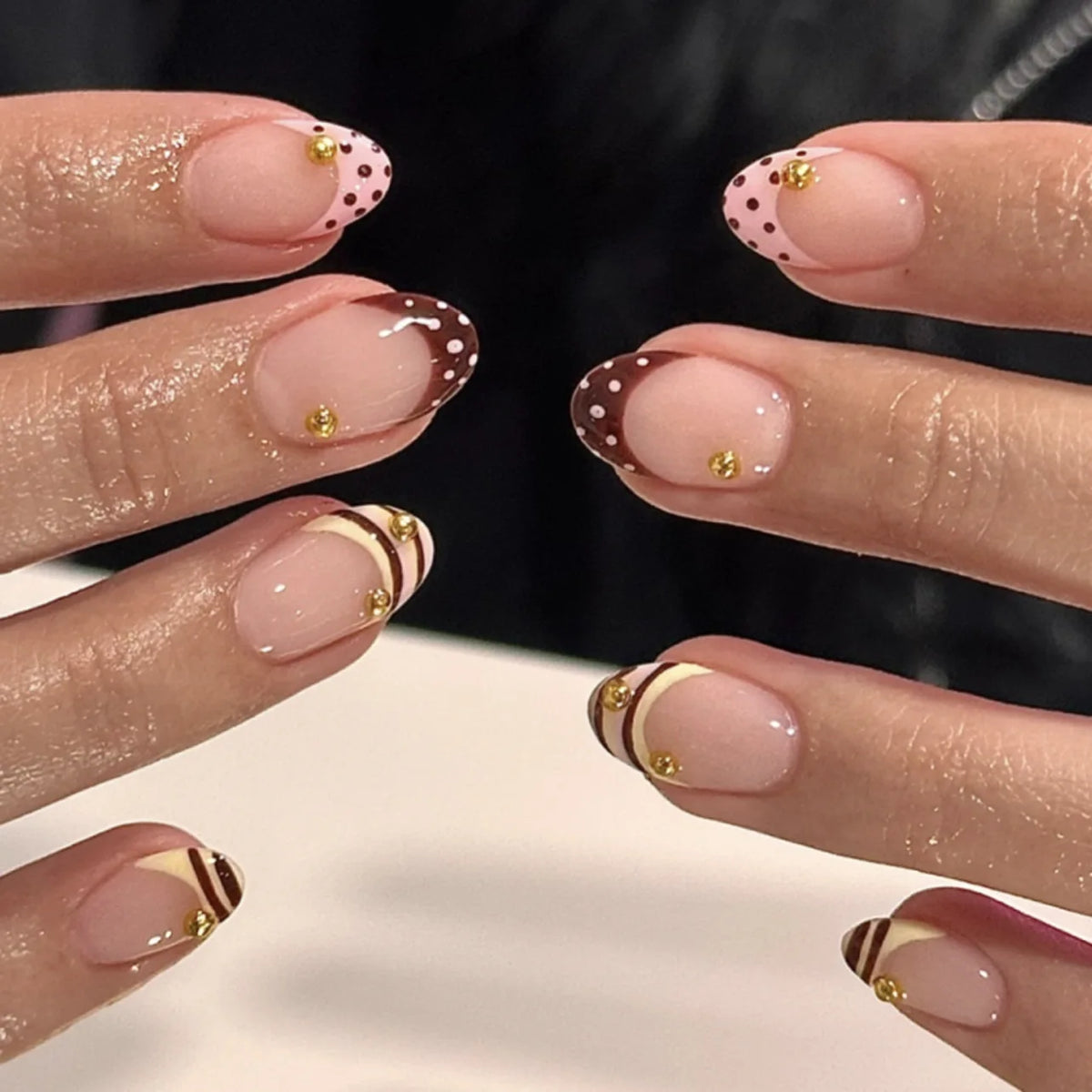 Gros plan sur des doigts manucurés montrant des kits de ongles fleurs à amande pressées avec pois roses et dorés.