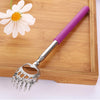 A silver stainless steel telescopic back scratcher with a purple handle resting on a wooden cutting board next to a white flo