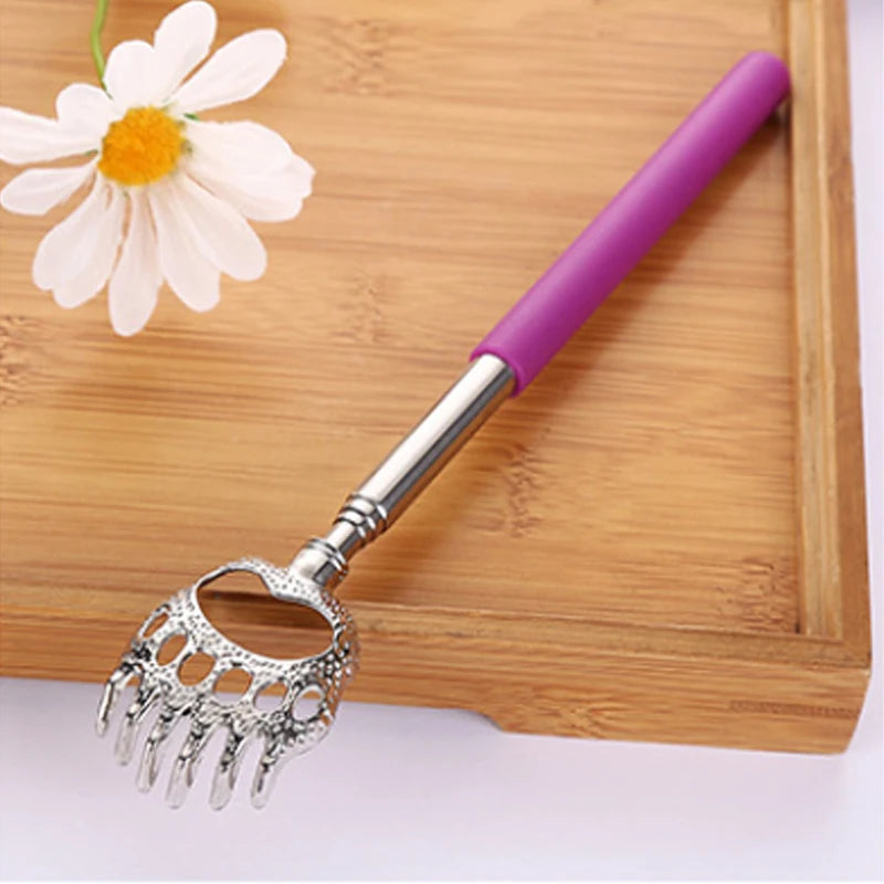A silver stainless steel telescopic back scratcher with a purple handle resting on a wooden cutting board next to a white flo