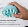 A hand holds a light blue wet and dry scalp massage brush with pointed bristles, demonstrating its use for cleaning and massa