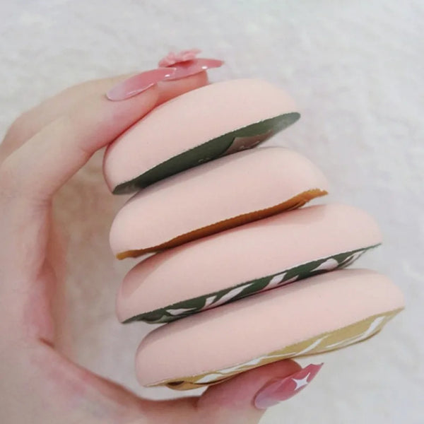 A hand holds a set of pink air cushion makeup puffs with green accents.