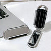 A silver portable compact comb with a black silicone bag and mirror is shown next to a laptop.