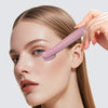 A woman is using a pink eye massage instrument on her eyelid to relieve tiredness and restore vitality.