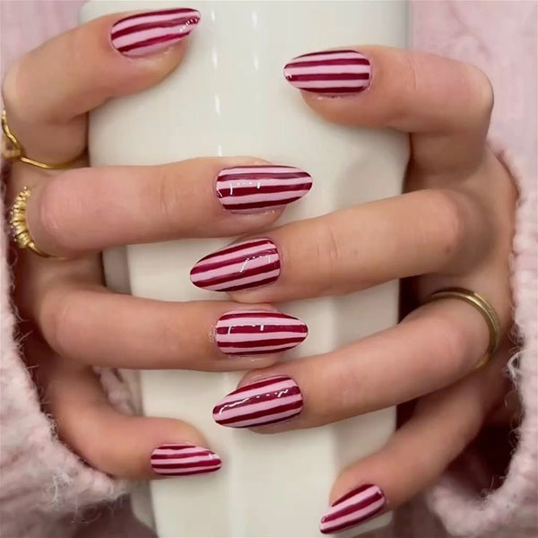 A hand displays red and pink striped press-on nails on fingers, set against a soft pink background.