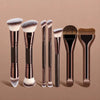 A set of seven professional makeup brushes with varying sizes and shades displayed on a neutral background.