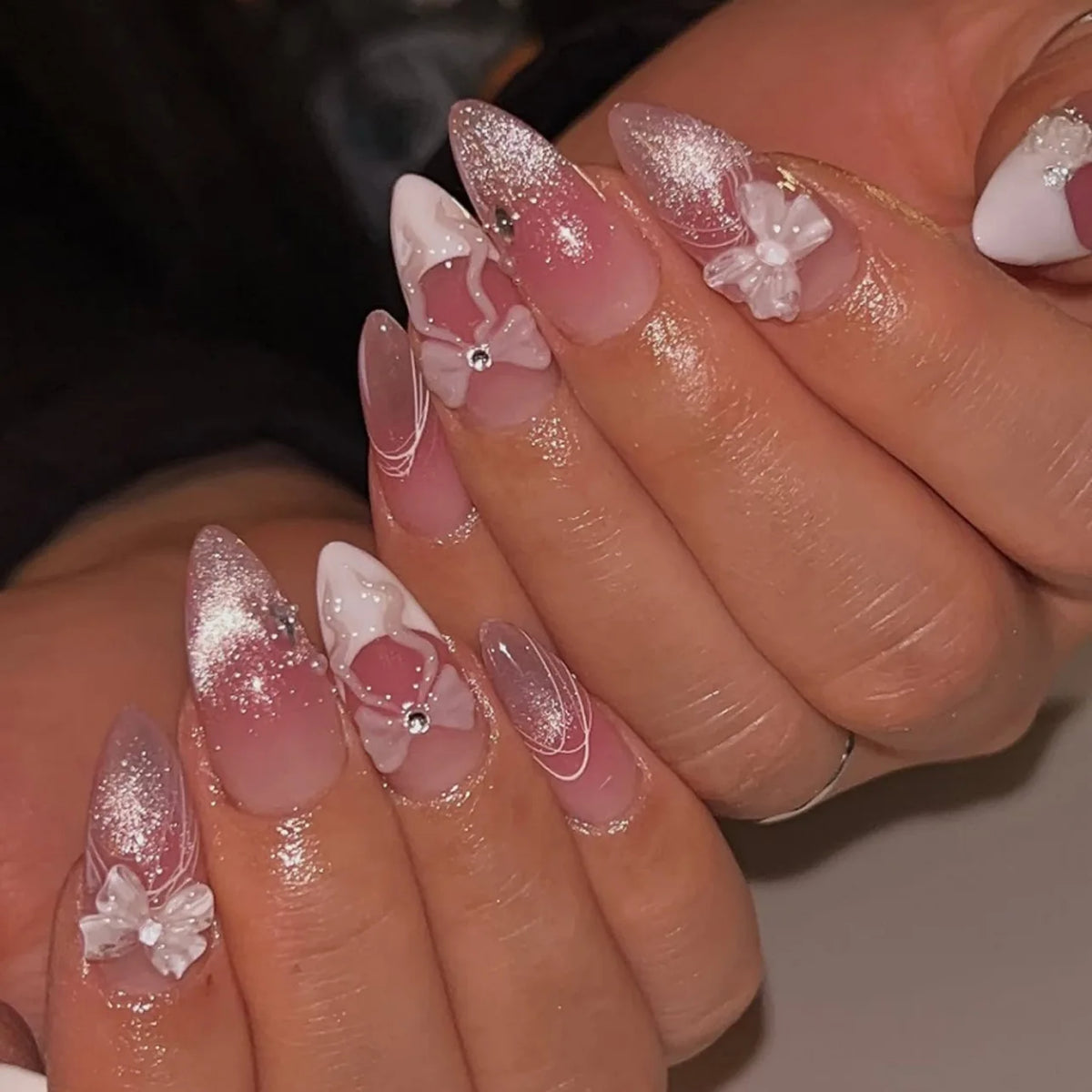 A close-up of hands displaying pink heart pearl press-on fake nails with glitter accents.