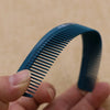 A hand holds a dark blue anti-static professional hair cutting comb, showing its serrated teeth and curved shape.