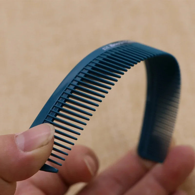 A hand holds a dark blue anti-static professional hair cutting comb, showing its serrated teeth and curved shape.