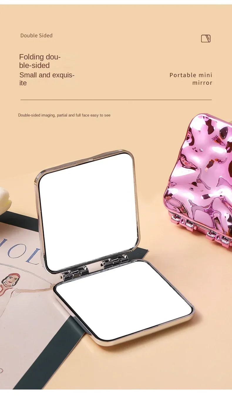 Un miroir de maquillage carré pliable ouvert à côté d'un mini-miroir rose et d'une boîte de produit cosmétique.