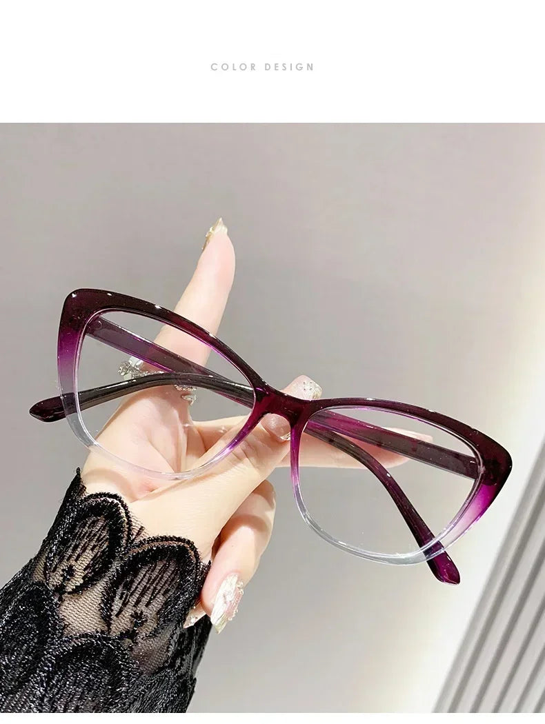 A hand holds a pair of purple cat eye reading glasses with clear frames against a light background.